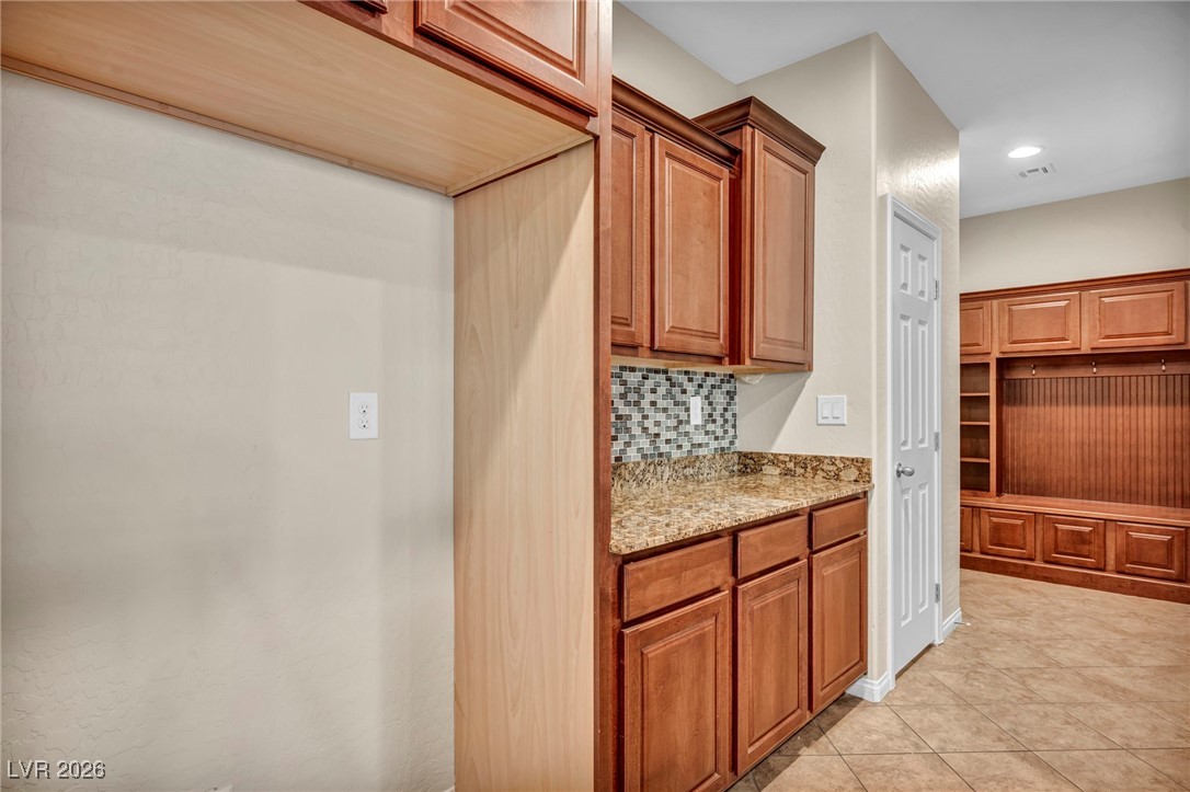 356 Aqua Springs Road Las Vegas, NV 89148 - Photo 17 of 39 Kitchen with light stone counters, brown cabinets, backsplash, recessed lighting, and light tile patterned floors