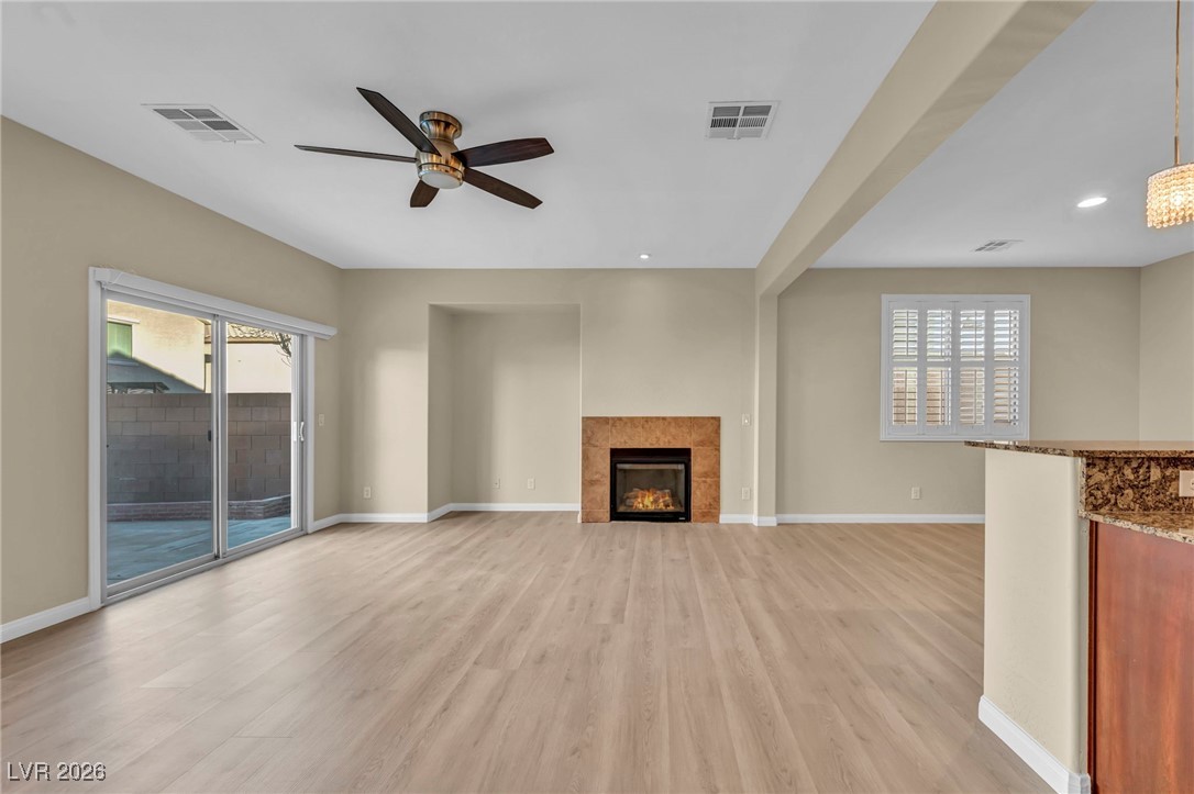 356 Aqua Springs Road Las Vegas, NV 89148 - Photo 19 of 39 Unfurnished living room with light wood-type flooring, a tile fireplace, a ceiling fan, healthy amount of natural light, and recessed lighting