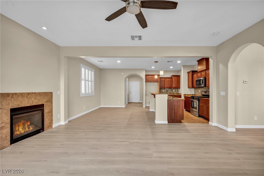 356 Aqua Springs Road Las Vegas, NV 89148 - Photo 4 of 39 Unfurnished living room featuring arched walkways, a tile fireplace, ceiling fan, recessed lighting, and light wood finished floors