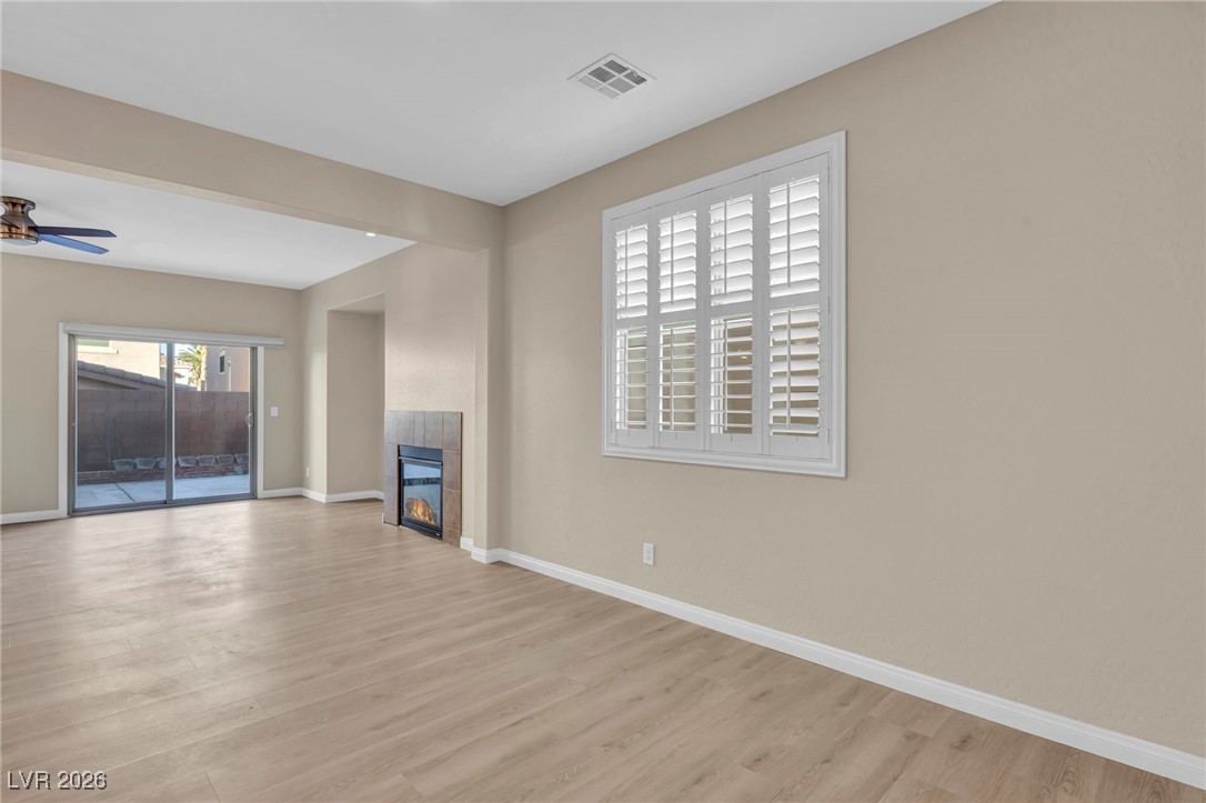 356 Aqua Springs Road Las Vegas, NV 89148 - Photo 7 of 39 Unfurnished living room featuring a tiled fireplace, light wood finished floors, and a ceiling fan