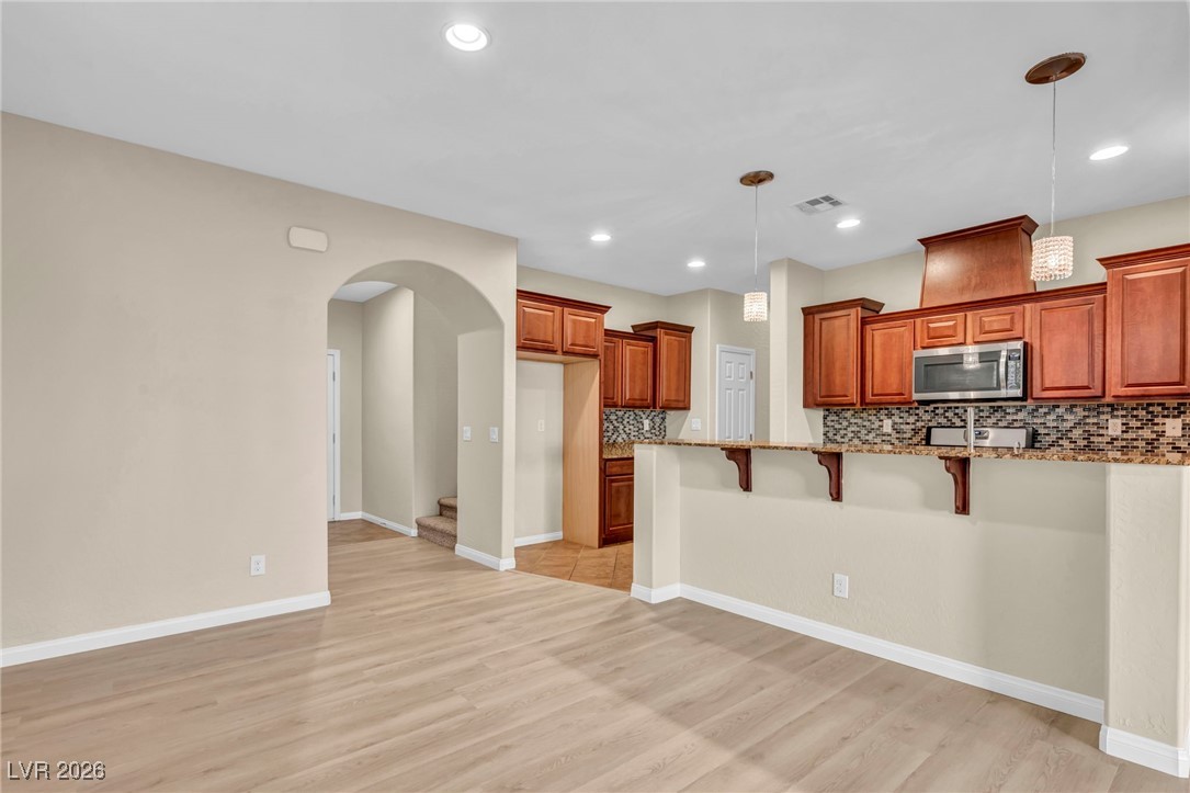 356 Aqua Springs Road Las Vegas, NV 89148 - Photo 8 of 39 Kitchen featuring tasteful backsplash, arched walkways, brown cabinetry, a kitchen bar, and pendant lighting