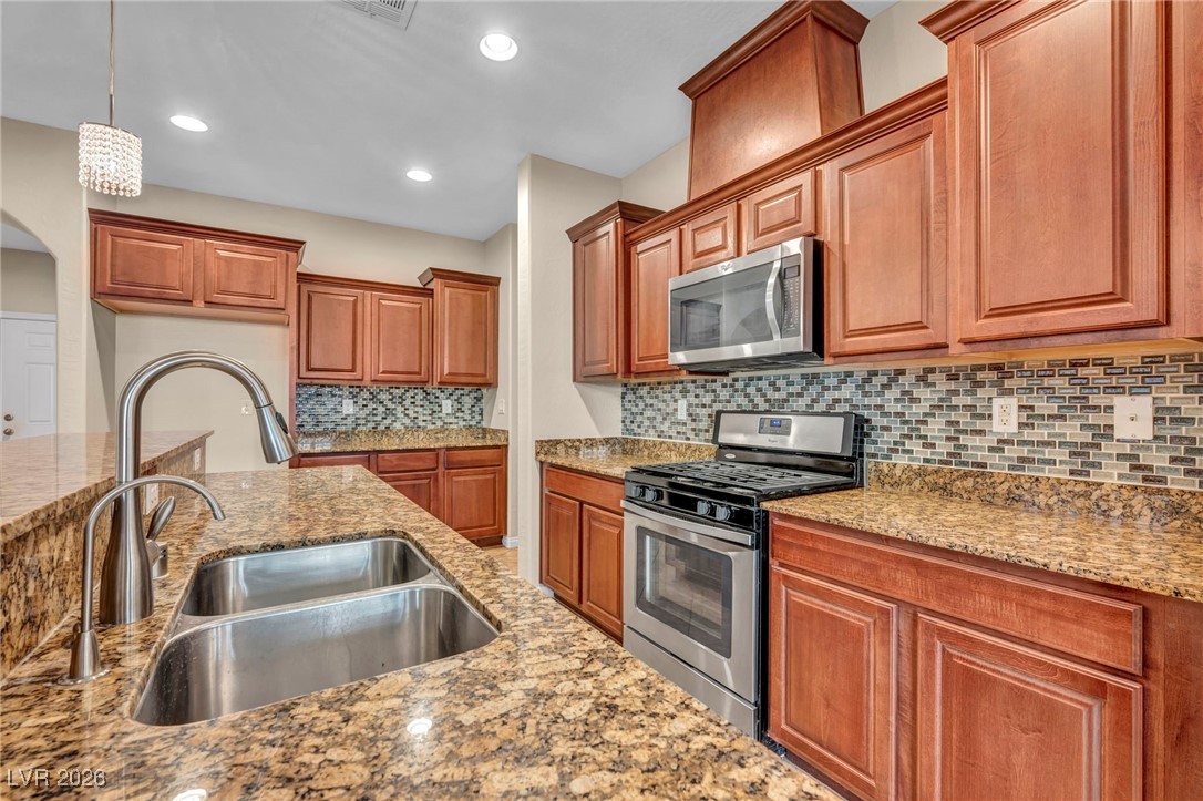 356 Aqua Springs Road Las Vegas, NV 89148 - Photo 10 of 39 Kitchen with appliances with stainless steel finishes, brown cabinets, light stone countertops, pendant lighting, and recessed lighting