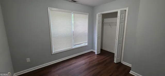 an empty room with wooden floor closet and windows