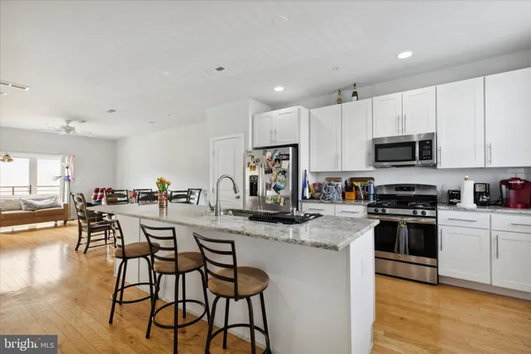 a kitchen with stainless steel appliances granite countertop a stove top oven a sink a dining table and chairs with wooden floor