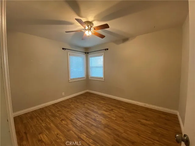 a view of an empty room with wooden floor and a fan