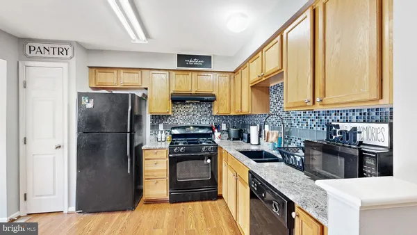 a kitchen with stainless steel appliances granite countertop a refrigerator a sink dishwasher a stove with wooden floor and cabinets next to a window