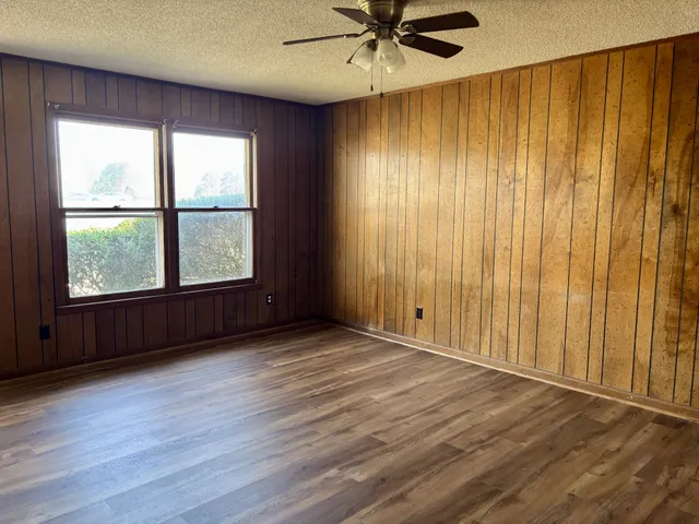 an empty room with wooden floor fan and windows