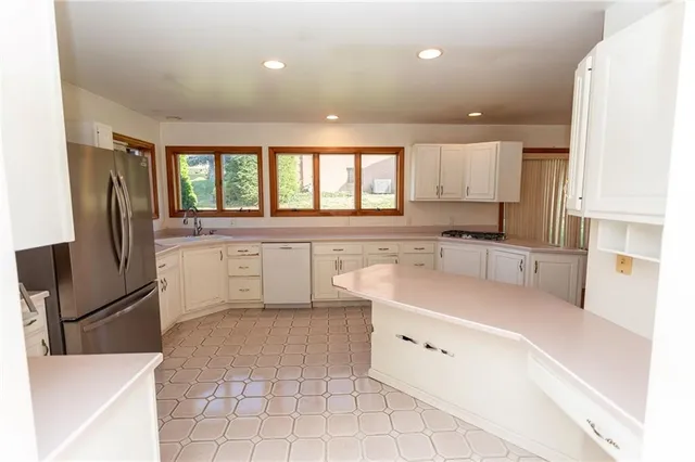 a large white kitchen with a sink a refrigerator and cabinets