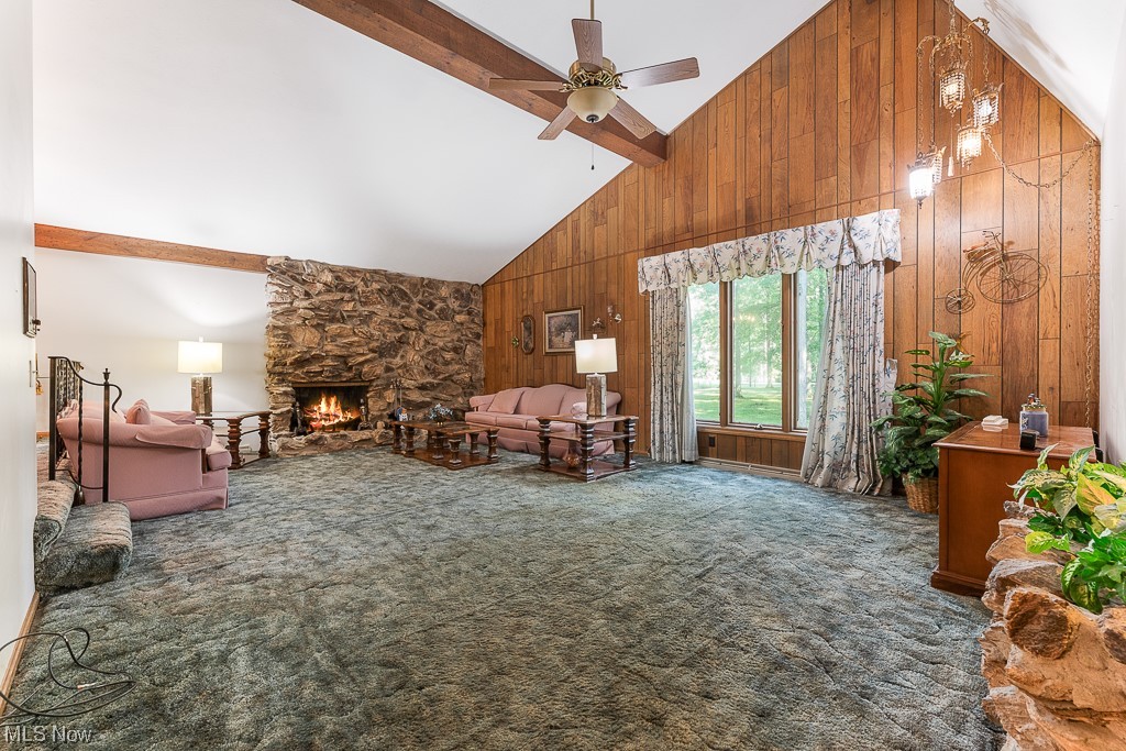 19235 West Middletown Road Beloit, OH 44609 - Photo 14 of 35 Living room featuring a fireplace, wood walls, light carpet, vaulted ceiling with beams, a high ceiling, and ceiling fan