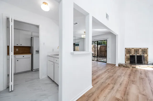 a view of a hallway to an empty room with wooden floor and a kitchen