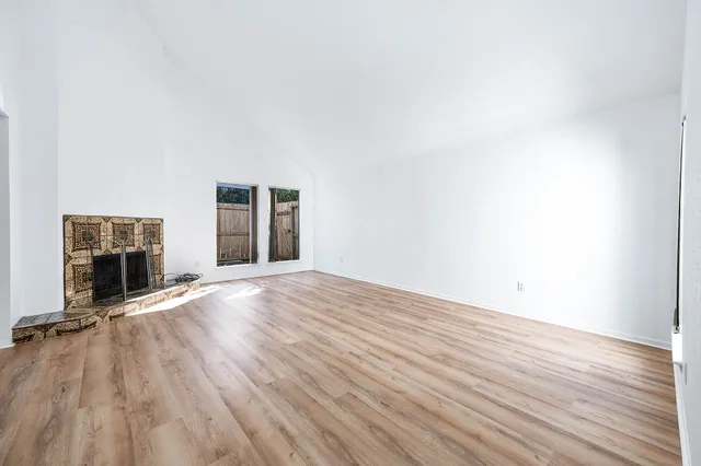 a view of an empty room with wooden floor fireplace and a window