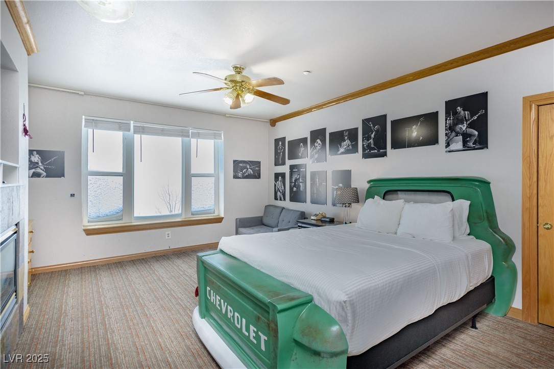 Carpeted bedroom with a ceiling fan, ornamental molding, and a glass covered fireplace