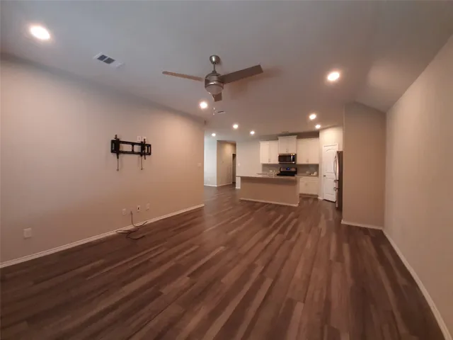 an empty room with wooden floor a ceiling fan kitchen view and windows