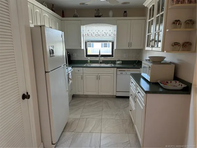 a kitchen with granite countertop a refrigerator a sink a stove and white cabinets