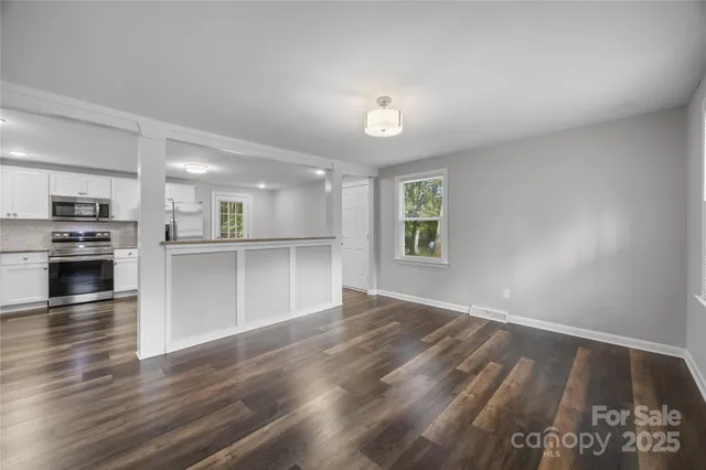 an empty room with wooden floor kitchen view and a window