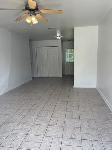 an empty room with chandelier fan and kitchen view