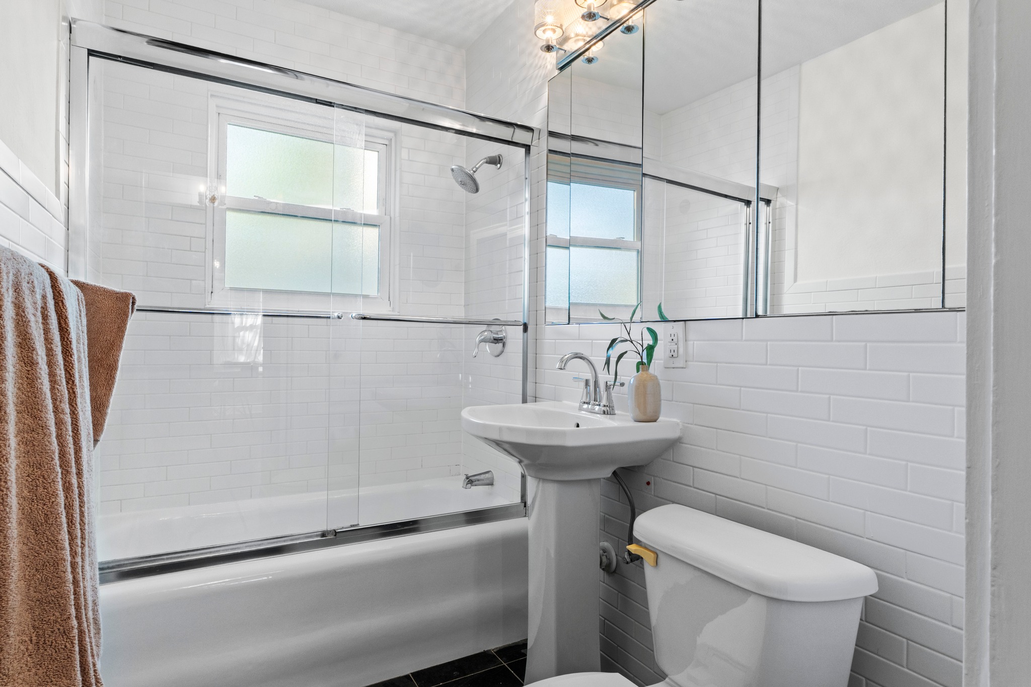 4802 Rowena Avenue Austin, TX 78751 - Photo 18 of 37 Bathroom featuring white subway tile, a pedestal sink, a bathtub with a glass shower enclosure, a toilet, and a medicine cabinet with integrated lighting.