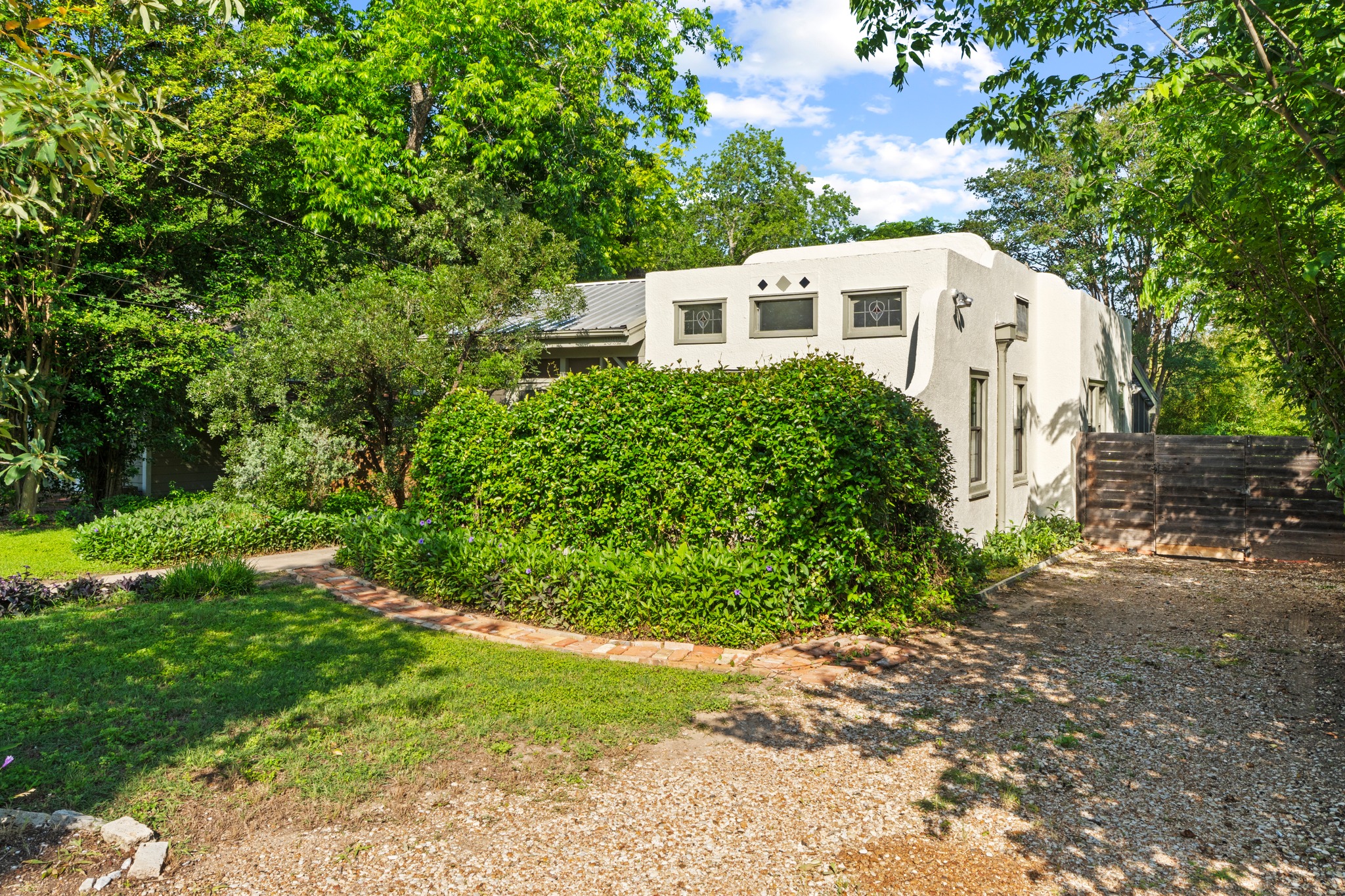 4802 Rowena Avenue Austin, TX 78751 - Photo 36 of 37 Stucco exterior residence featuring decorative windows, a gravel driveway, and a brick-edged pathway.