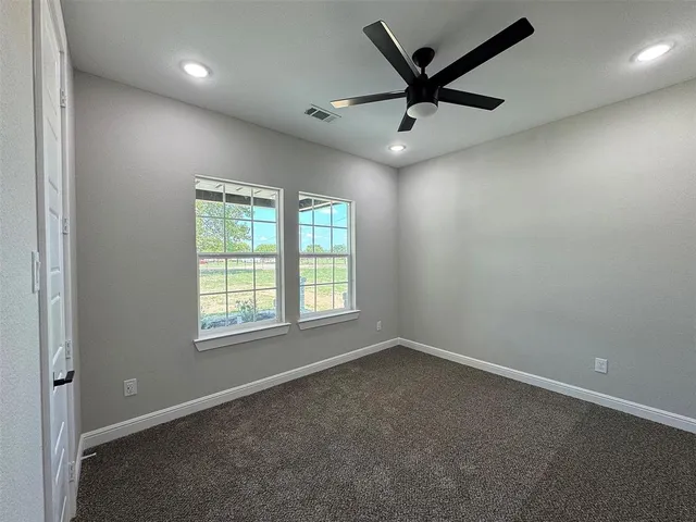 an empty room with ceiling fan and windows