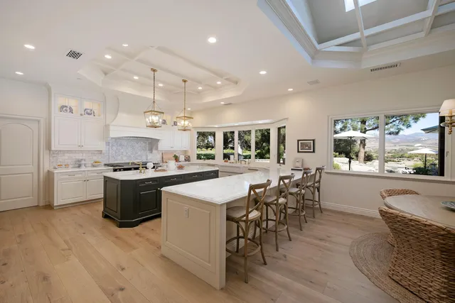 a large white kitchen with a large counter top space a sink stainless steel appliances and cabinets