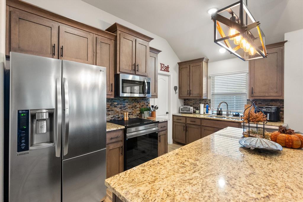 4021 Grove Valley Road Midlothian, TX 76065 - Photo 17 of 27 Kitchen featuring appliances with stainless steel finishes, decorative backsplash, light stone countertops, lofted ceiling, and hanging light fixtures