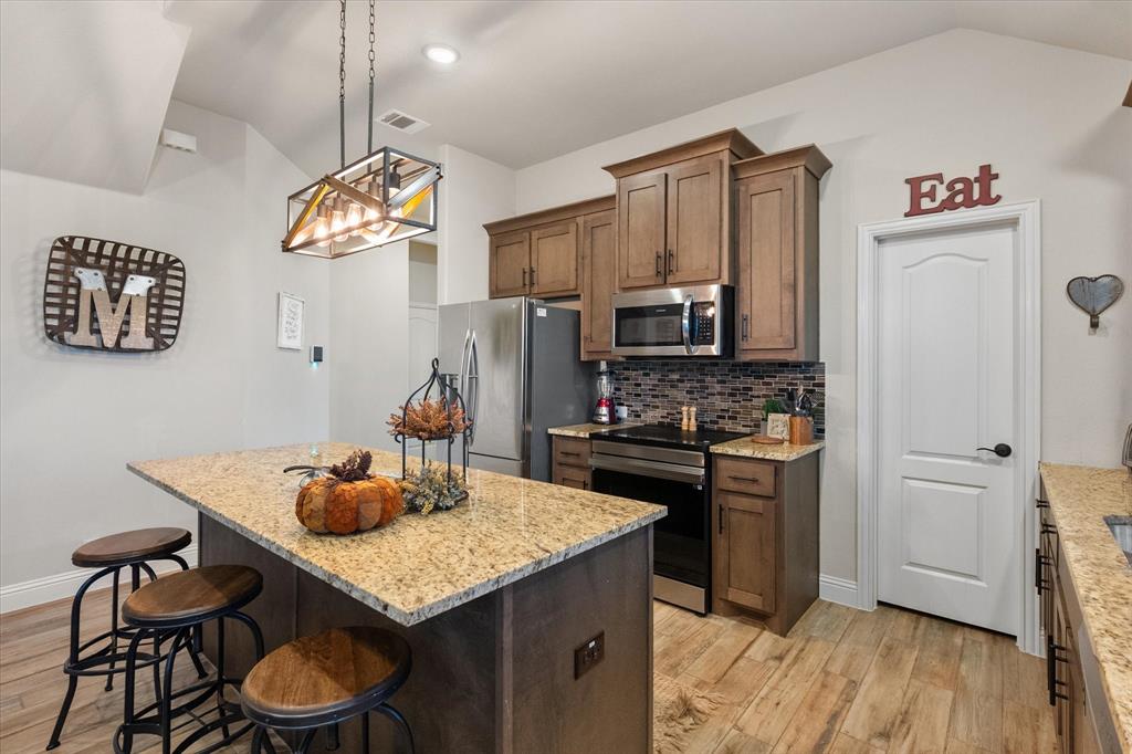 4021 Grove Valley Road Midlothian, TX 76065 - Photo 18 of 27 Kitchen featuring tasteful backsplash, stainless steel appliances, a center island, a breakfast bar area, and decorative light fixtures