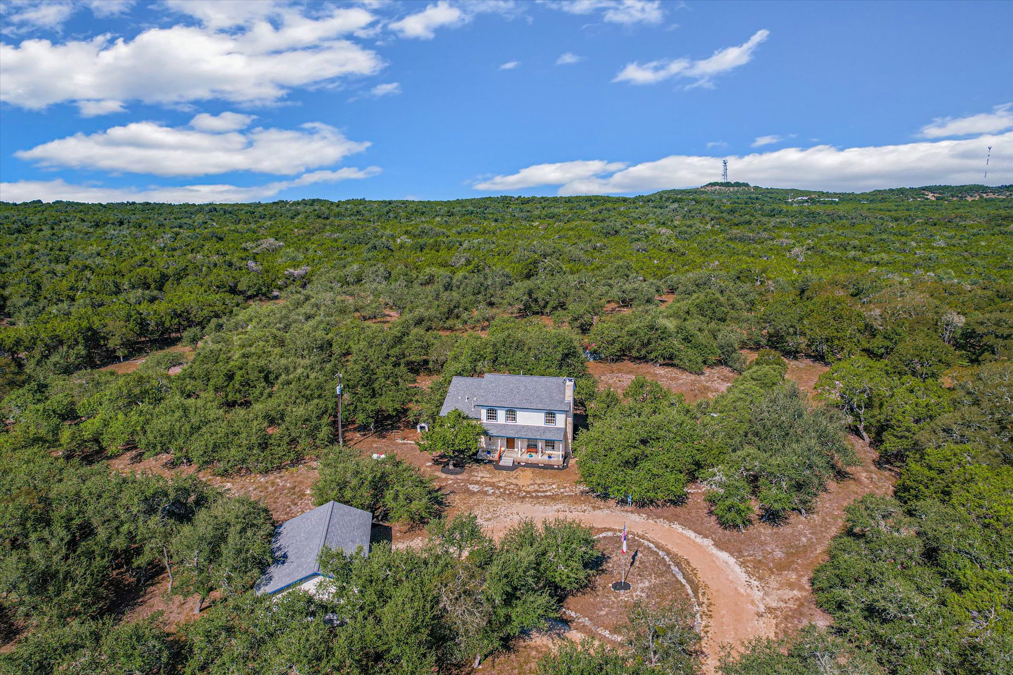 401 North Rainbow Ranch Road Wimberley, TX 78676 - Photo 38 of 39 Mature trees surround this private hillside retreat under expansive blue skies.