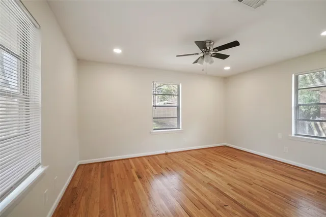 an empty room with wooden floor ceiling fan and windows