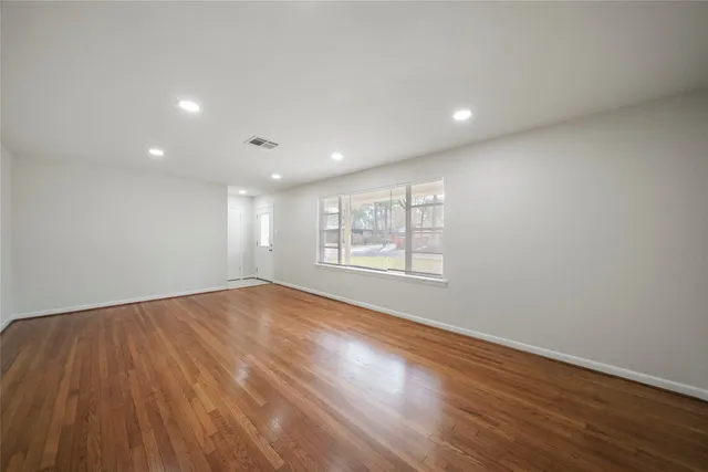 a view of an empty room with wooden floor and a window