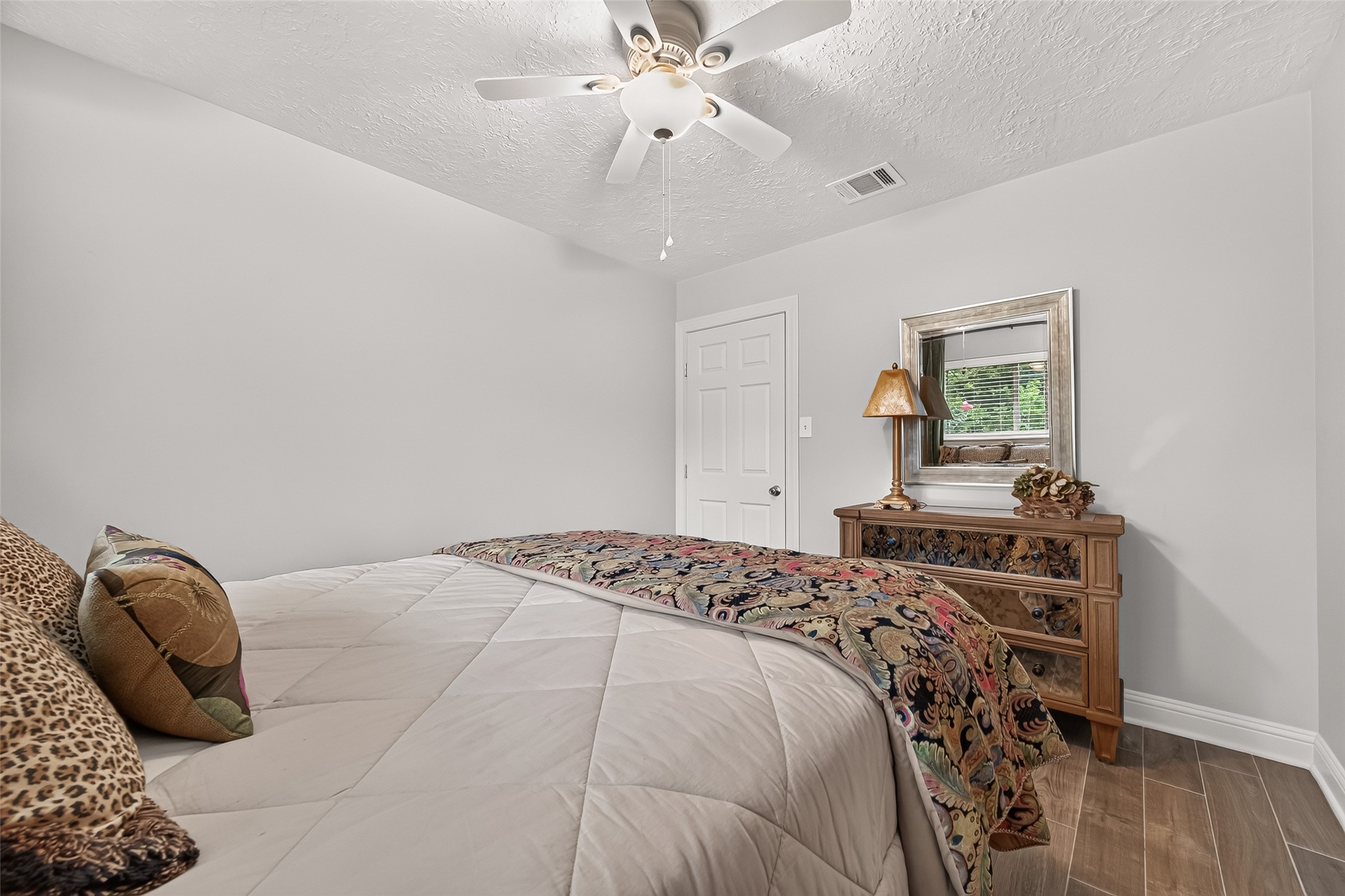 24719 Wilderness Road Spring, TX 77380 - Photo 22 of 42 This cozy bedroom features a ceiling fan, neutral walls, and wood-like ceramic tile flooring, creating a warm and inviting atmosphere.