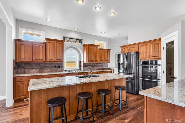 a kitchen with stainless steel appliances granite countertop a refrigerator a stove and a sink with wooden cabinets