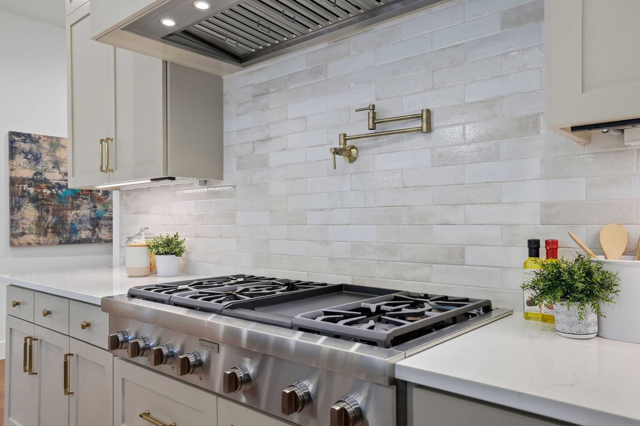 6611 Lexington Road Austin, TX 78757 - Photo 12 of 37 Gourmet kitchen featuring a professional-grade stainless steel range with griddle, a decorative tiled backsplash, a brass pot filler, under-cabinet lighting, and light-toned cabinetry with brass hardware