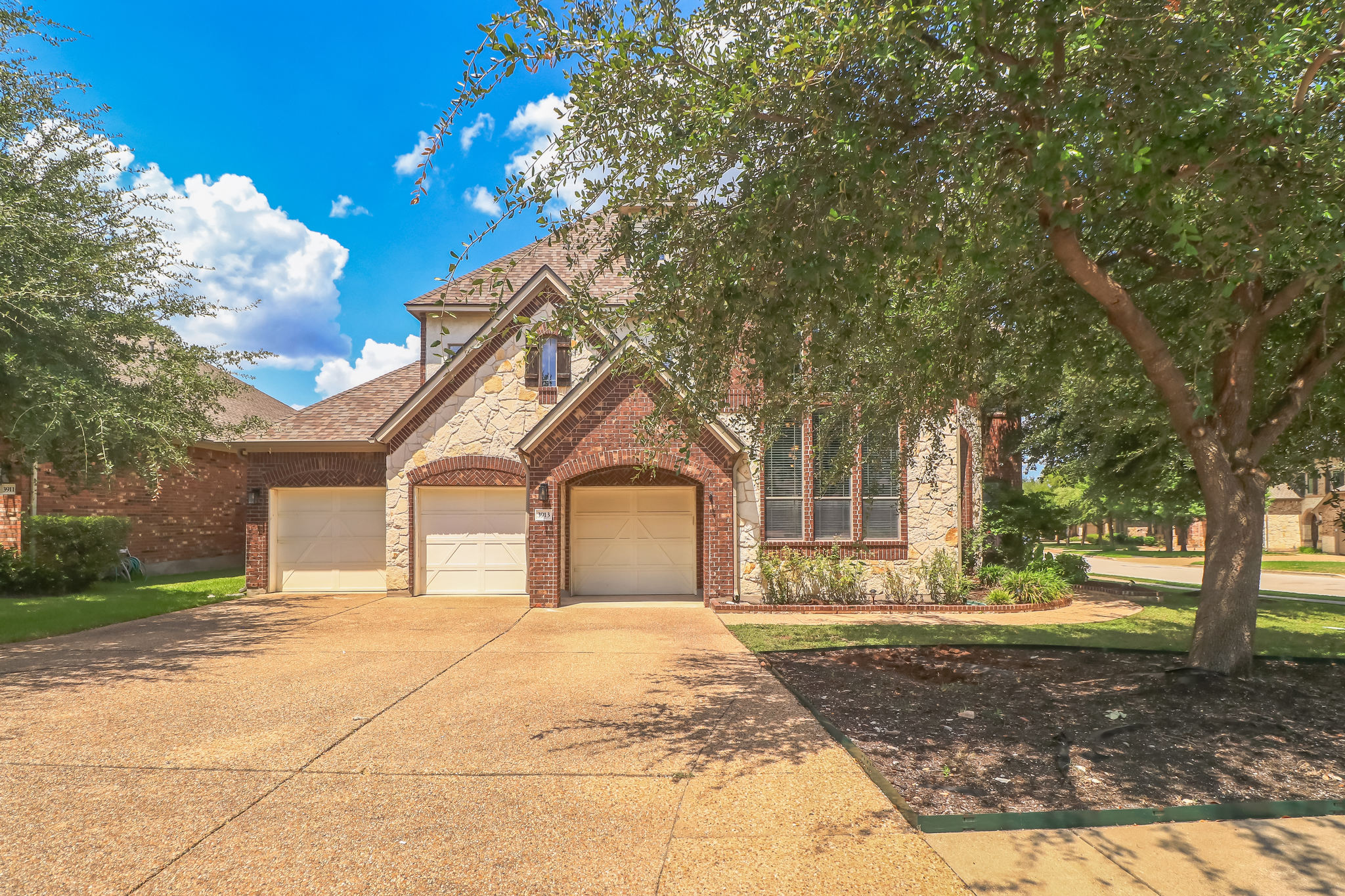 Mature trees frame a classic brick and stone facade complete with a multi-car garage.