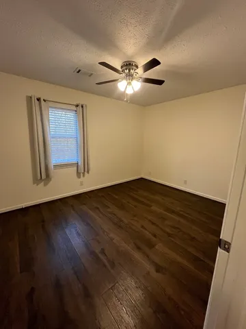 a view of an empty room with wooden floor and a ceiling fan
