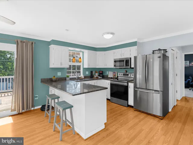 a kitchen with stainless steel appliances granite countertop a stove top oven a sink a dining table and chairs with wooden floor