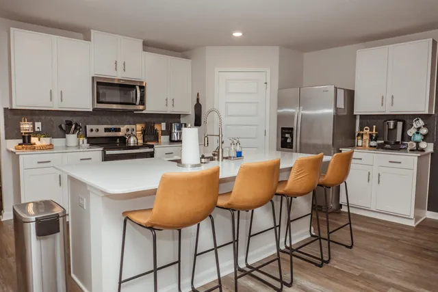 a kitchen with stainless steel appliances granite countertop a dining table chairs refrigerator and microwave