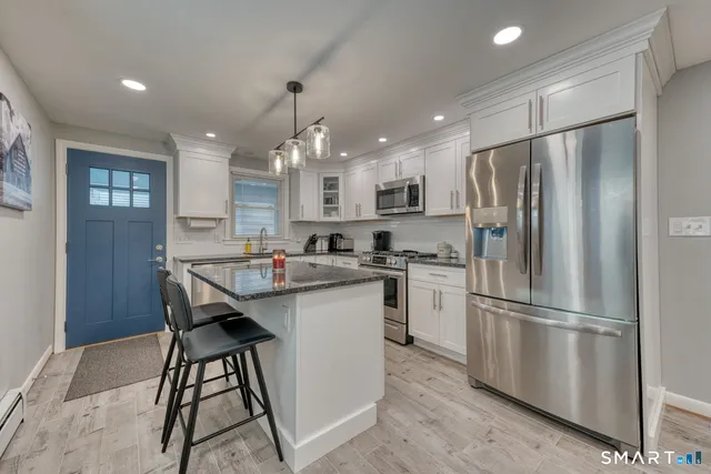 a kitchen with stainless steel appliances granite countertop a refrigerator a sink dishwasher a stove and a refrigerator with wooden floor