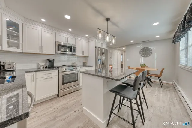 a kitchen with stainless steel appliances kitchen island granite countertop a stove a sink a refrigerator and white cabinets with wooden floor