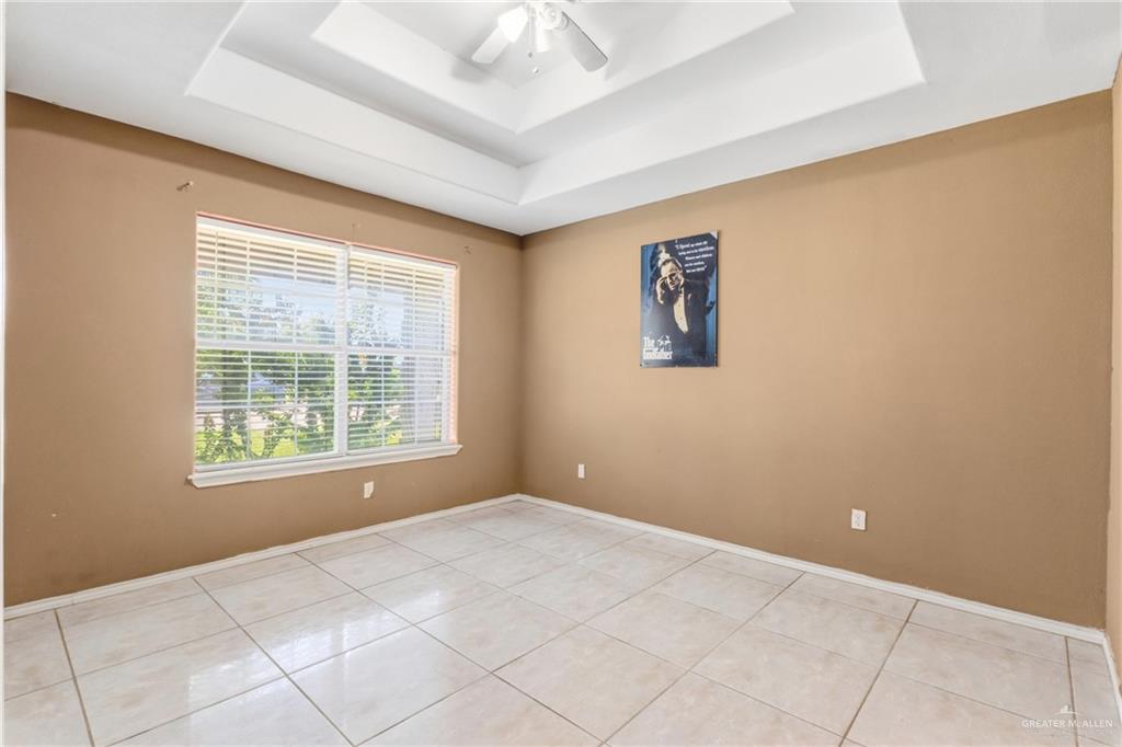 402 Mockingbird Lane Edcouch, TX 78538 - Photo 9 of 25 Spacious room featuring a tray ceiling, ceiling fan, large window with horizontal blinds, neutral wall tones, and tile flooring