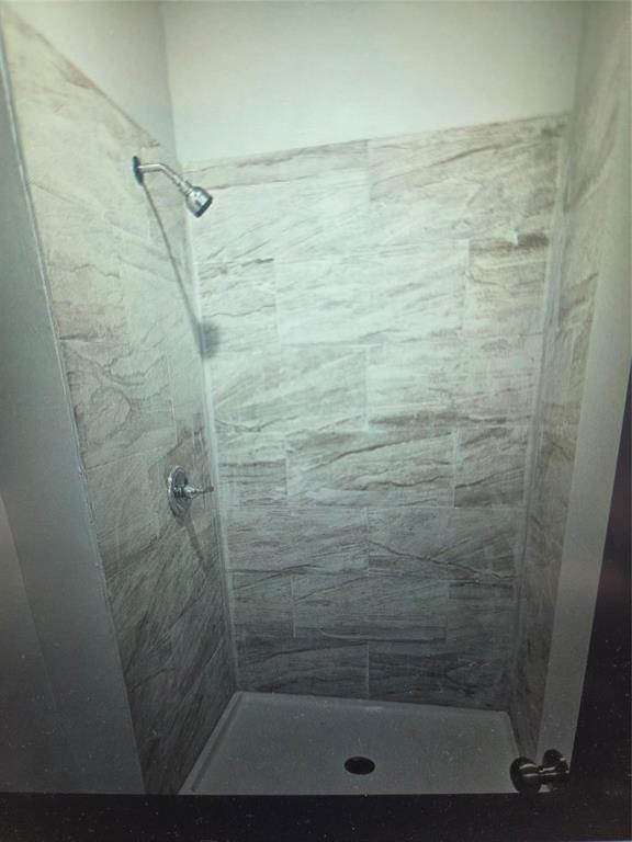 508 Allen Avenue Bonham, TX 75418 - Photo 5 of 10 Shower enclosure featuring light-toned, rectangular wall tiles with naturalistic veining, a chrome shower head, and a chrome single-handle control