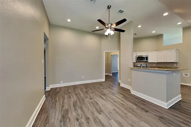 a view of an empty room with wooden floor and a ceiling fan