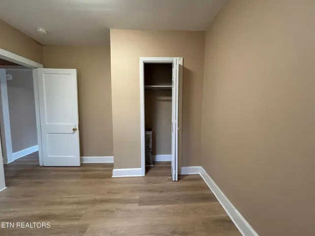 a view of an empty room with wooden floor and closet