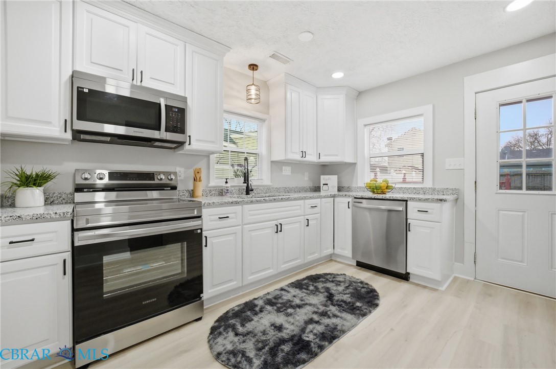 733 Spruce Street Hampton, VA 23661 - Photo 8 of 29 Kitchen featuring stainless steel appliances, white cabinetry, light stone countertops, light wood-style floors, and a textured ceiling