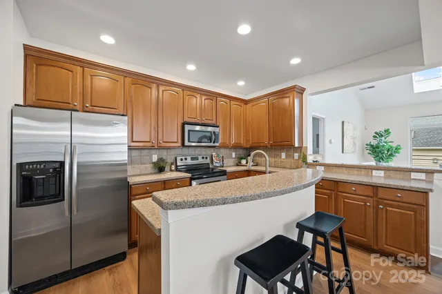 a kitchen with stainless steel appliances granite countertop a refrigerator a sink a stove a dining table and chairs