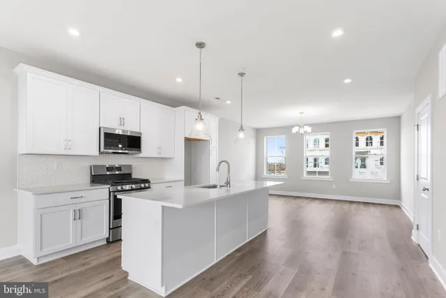 a large kitchen with stainless steel appliances granite countertop a stove a sink dishwasher a refrigerator white cabinets and wooden floor next to a window