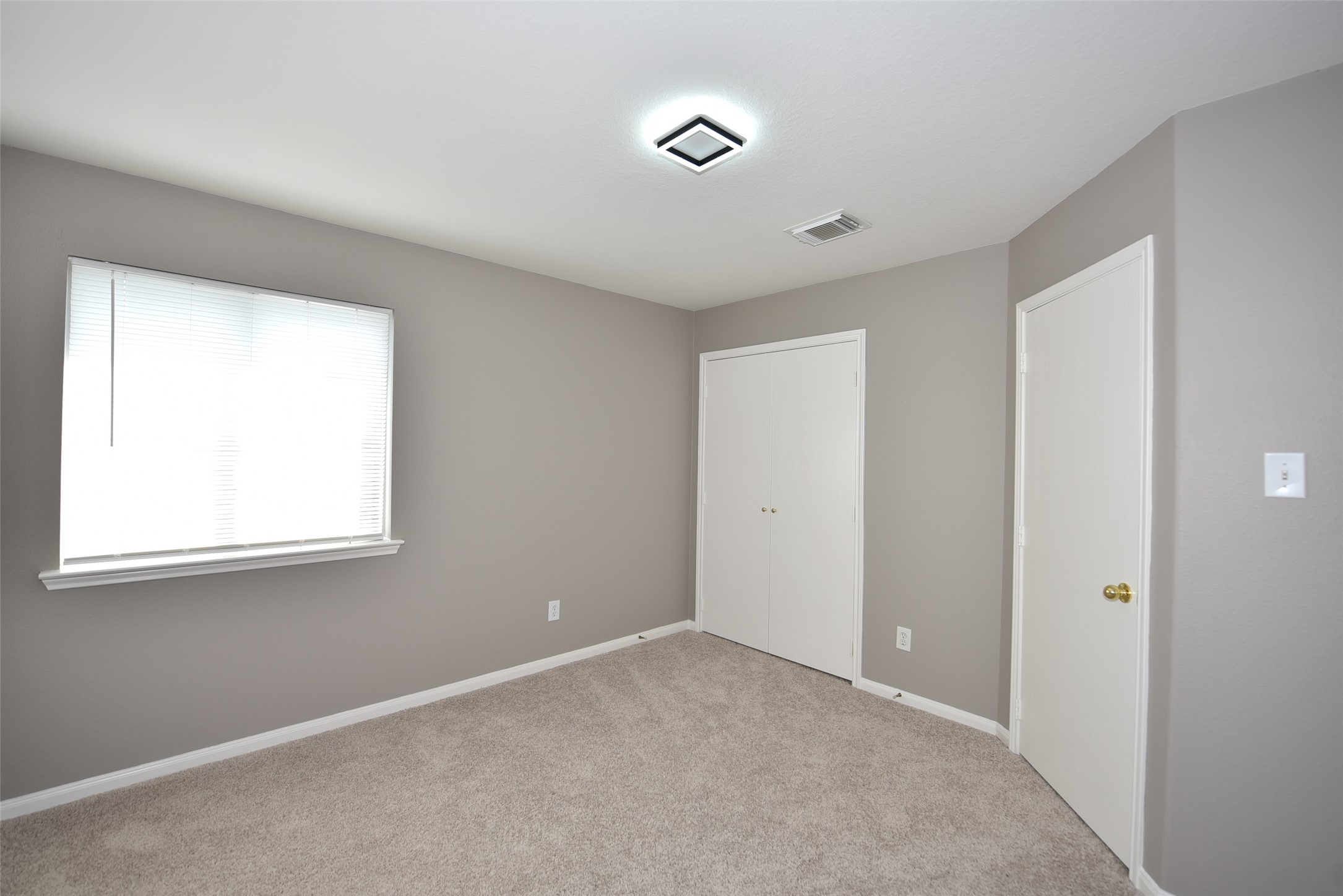 9611 Babbling Spring Court Tomball, TX 77375 - Photo 21 of 31 This room features neutral gray walls, a plush carpet, and a window with blinds, offering natural light. It includes a closet with white doors and a simple ceiling light fixture, creating a clean and cozy space.