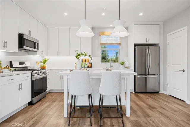 a kitchen with stainless steel appliances kitchen island granite countertop a refrigerator a stove a sink dishwasher a oven with a dining table and chairs with wooden floor