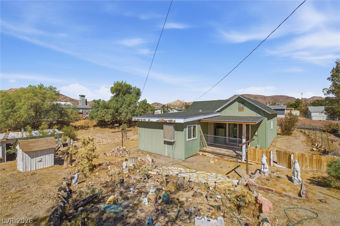 405 Main Street Beatty, NV 89003 - Photo 22 of 28 A charming green residence with a covered front porch, set against a backdrop of hills and mature trees.