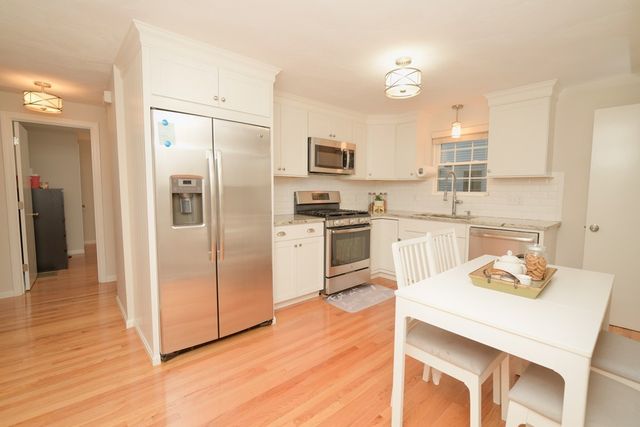 a kitchen with stainless steel appliances a refrigerator a stove a sink and white cabinets with wooden floor