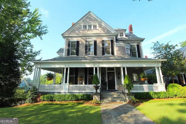 a view of a white house with a large windows and a yard with plants and large trees